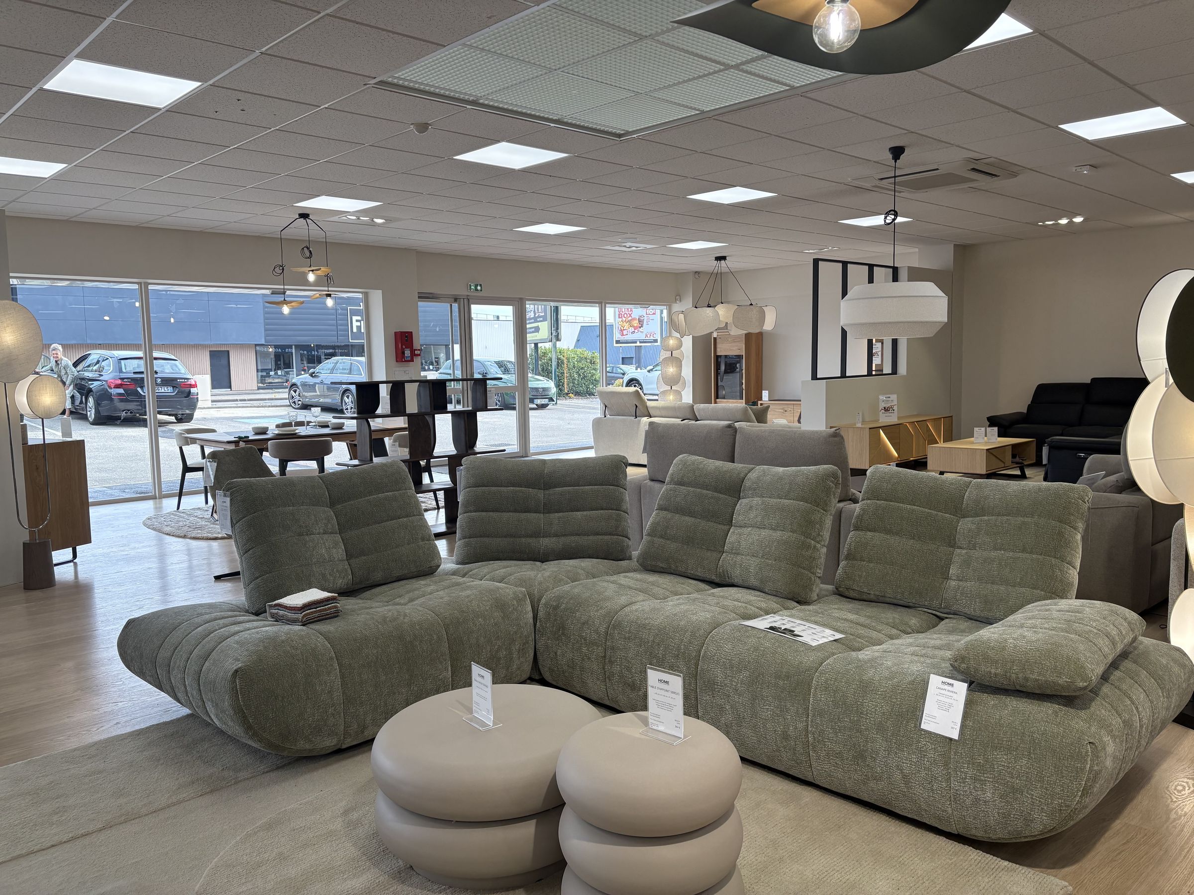 Canapé modulable vert sauge et poufs en tissu dans un grand espace lumineux