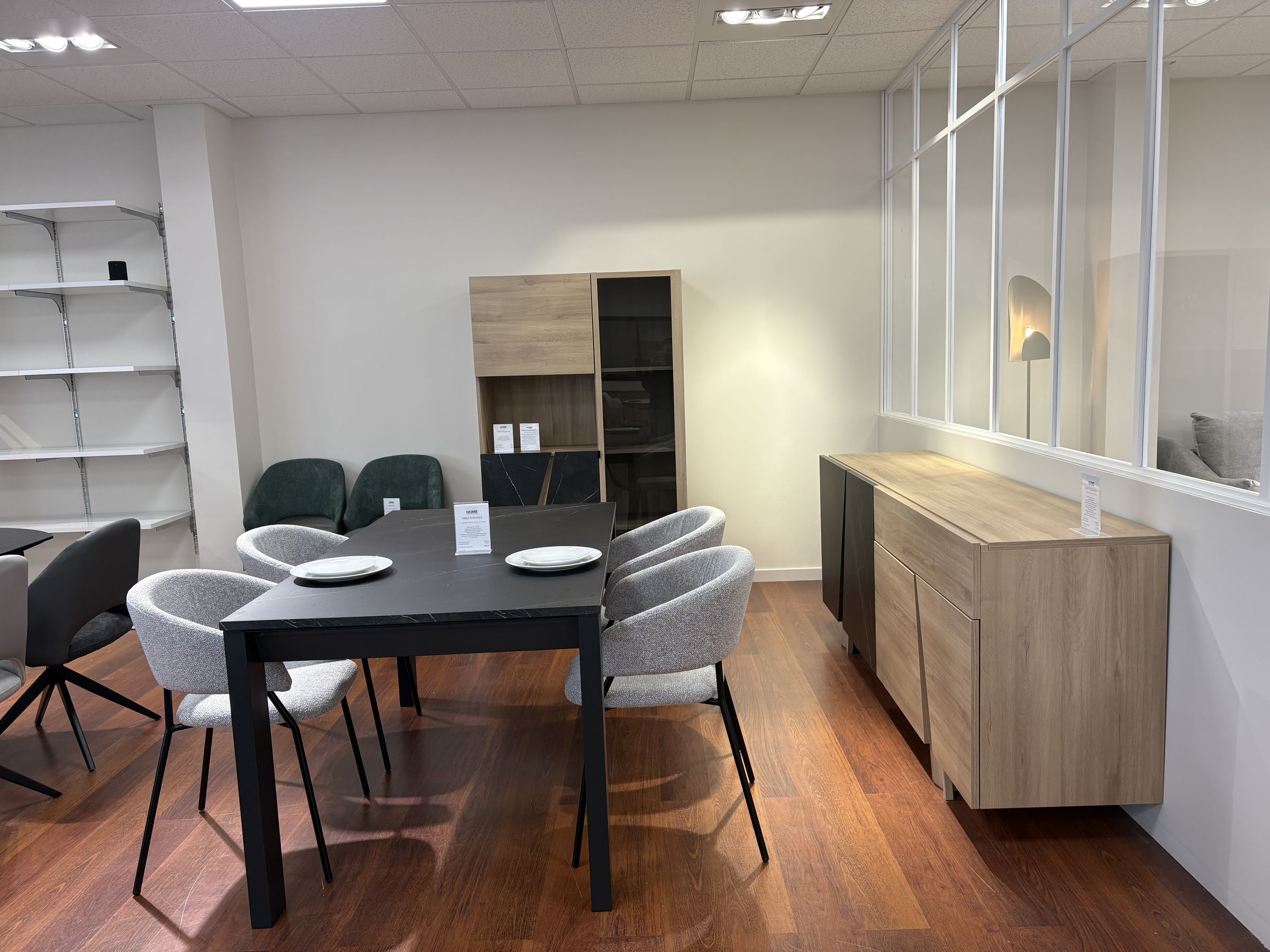 Table noire, chaises en tissu gris et buffet en chêne devant une verrière
